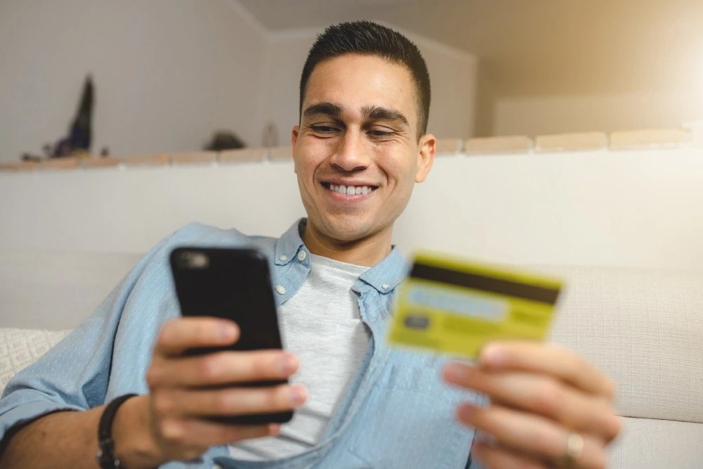 Joven sosteniendo su tarjeta bancaria y celular