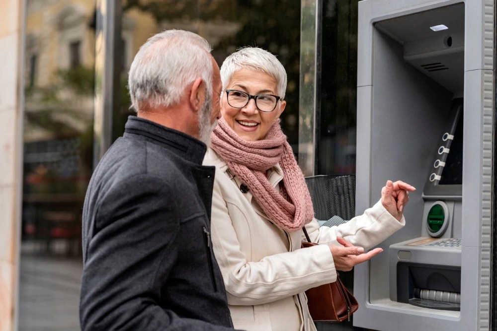 Adultos mayores haciendo retiros en efectivo en cajero automático.