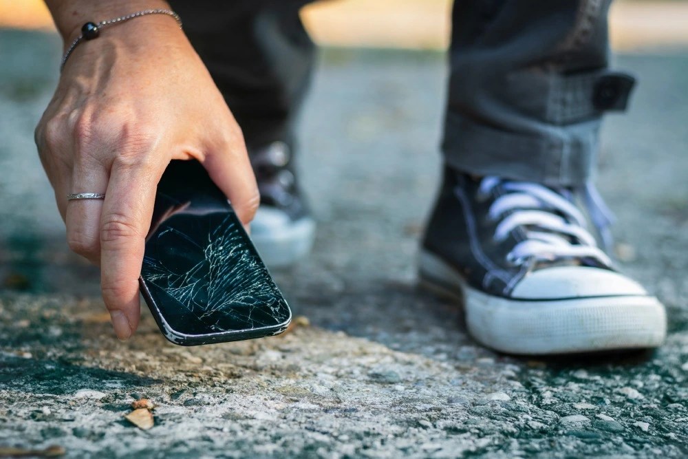 Seguro de celular: Hombre recogiendo celular roto del piso.