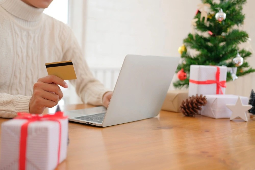 Persona con tarjeta bancaria en mano haciendo compras en línea para navidad.