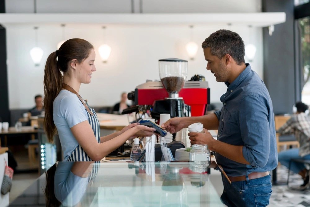 Persona pagando con tarjeta de débito en cafetería.