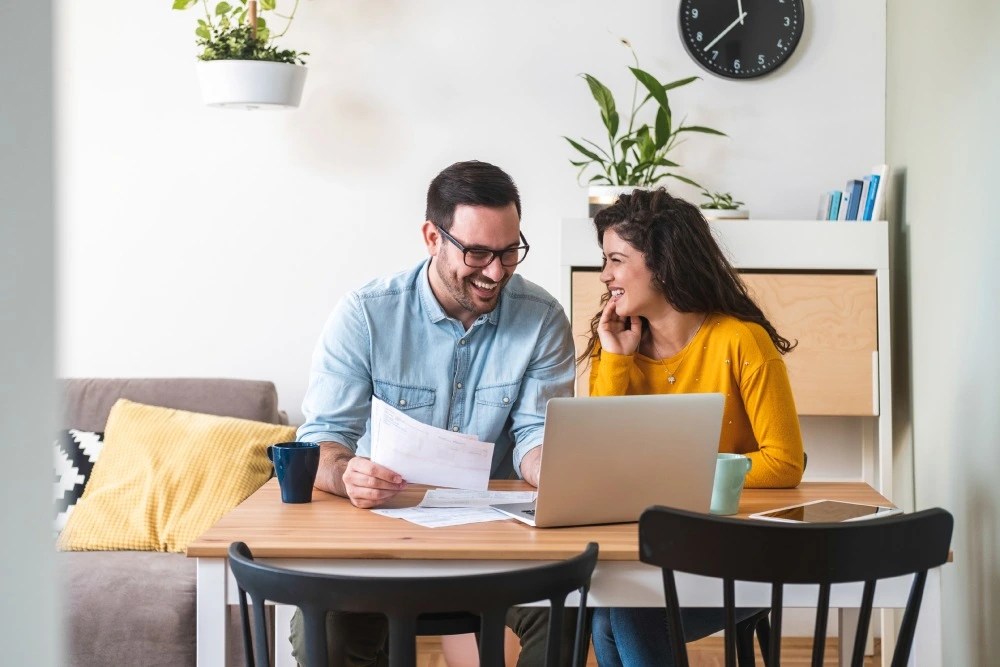 Pareja en computadora contentos aplicando estrategias para salir de deudas.