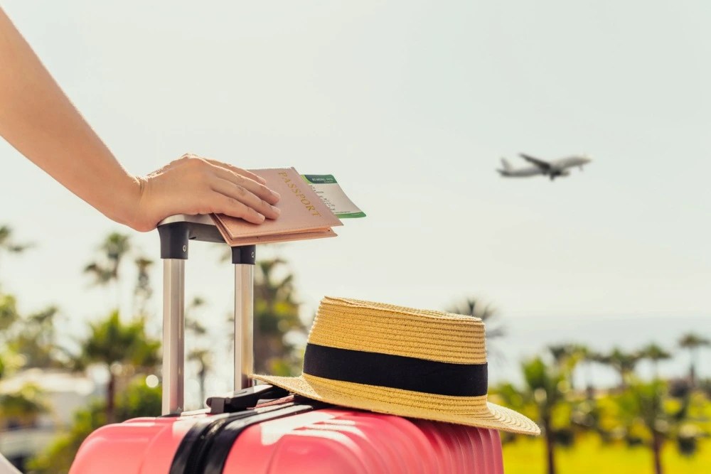 Persona de vacaciones con maleta y pasaje de avión.