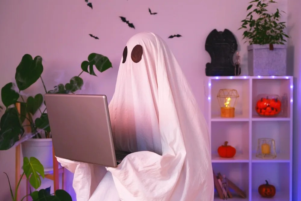 Persona disfrazada de fantasma sosteniendo un computador