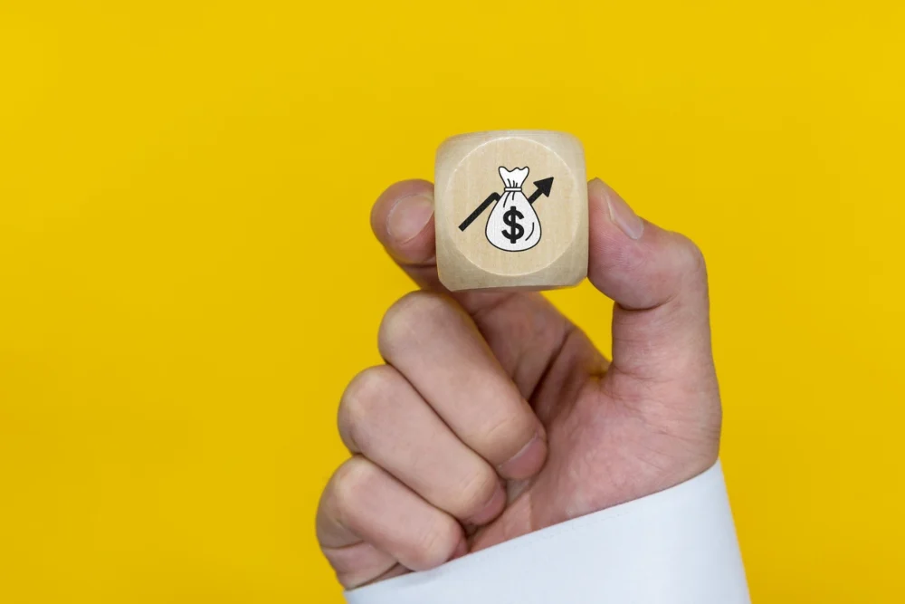 Mano sosteniendo un dado con un dibujo de dolar y flecha creciente