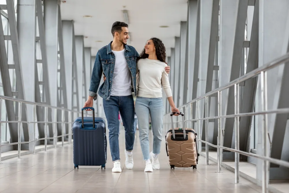 Pareja caminando en el aeropuertos con sus maletas para ir de vacaciones