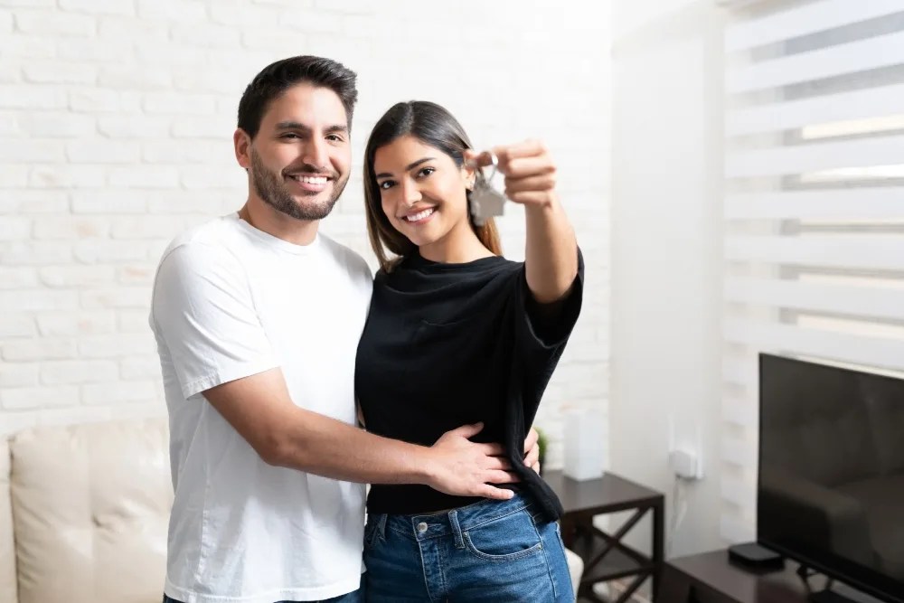 Pareja sosteniendo las llaves de la casa, dentro de su nuevo hogar