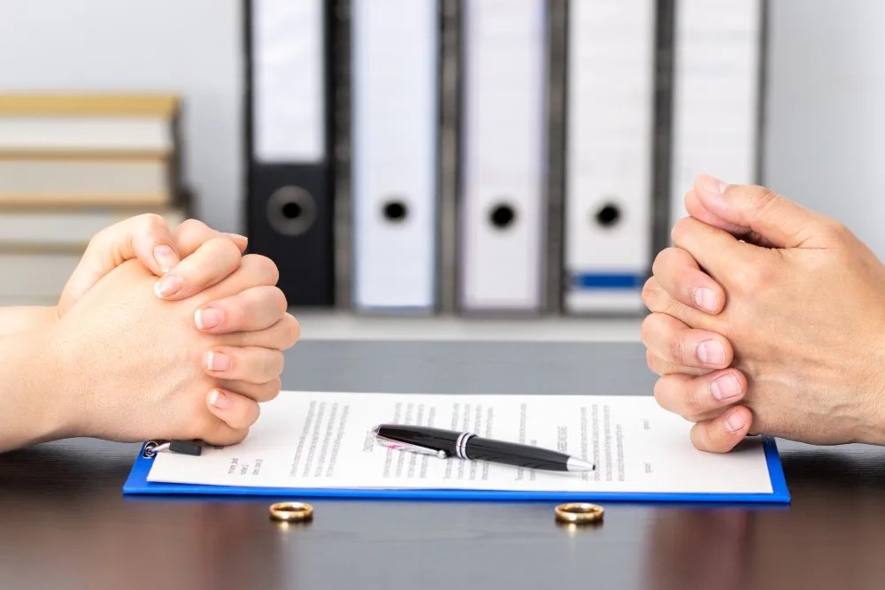 manos de 2 personas sobre documento y argollas de matrimonio