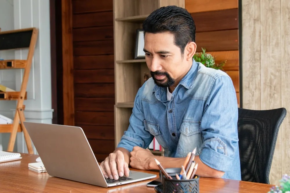 Hombre buscando en su computadora qué es el CAT en un crédito hipotecario