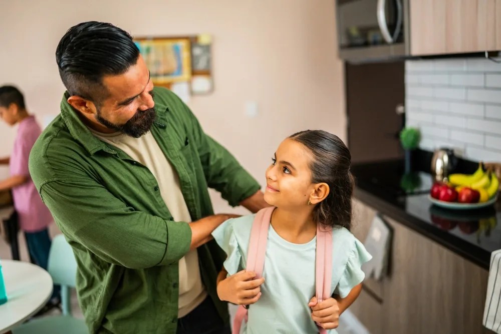 Seguro educativo: Padre preparando a hija para que vaya a la escuela