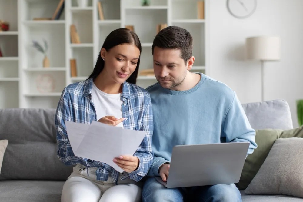 Pareja con documento y computador en mano revisando tabla de comisiones de crédito hipotecario
